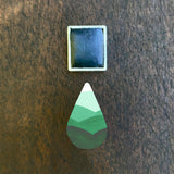 Emerald watercolour half pan above a droplet shaped ombre swatch in Emerald watercolour paint, on a rustic dark wooden background.