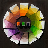 Three watercolour half pans in Pumpkin, Tree frog & Purple, surrounded by swatches that make up a colour wheel of the Trick or Treat colourway.